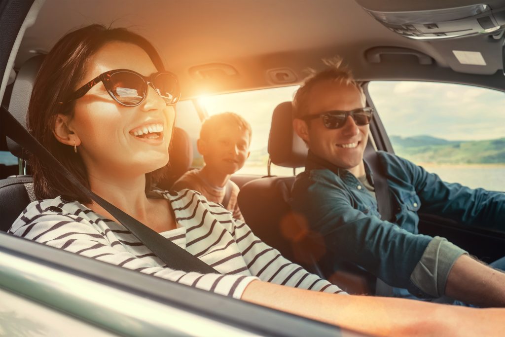 Family smiling, enjoying a road trip with sun shining in through the window of the SUV